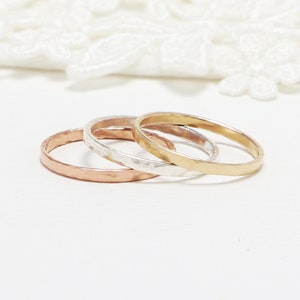 May include: Three thin hammered metal rings stacked together. The top ring is gold, the middle ring is silver, and the bottom ring is rose gold.