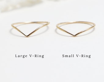 May include: Two gold V-shaped rings, one larger and one smaller. The rings are simple and delicate, with a smooth finish.