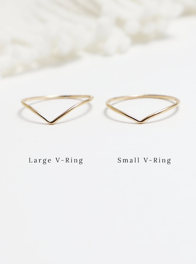 May include: Two gold V-shaped rings, one larger and one smaller. The rings are simple and delicate, with a smooth finish.