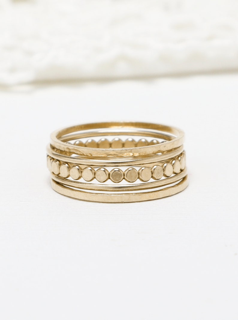 Pu&ograve; includere: Set di cinque anelli impilabili in oro. Gli anelli sono sottili e delicati, con un anello che presenta una fila di piccole perle rotonde.