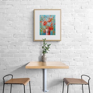 May include: A framed abstract painting of a bouquet of red flowers in a white vase against a blue background. The painting is hanging on a white brick wall above a wooden table with two chairs.