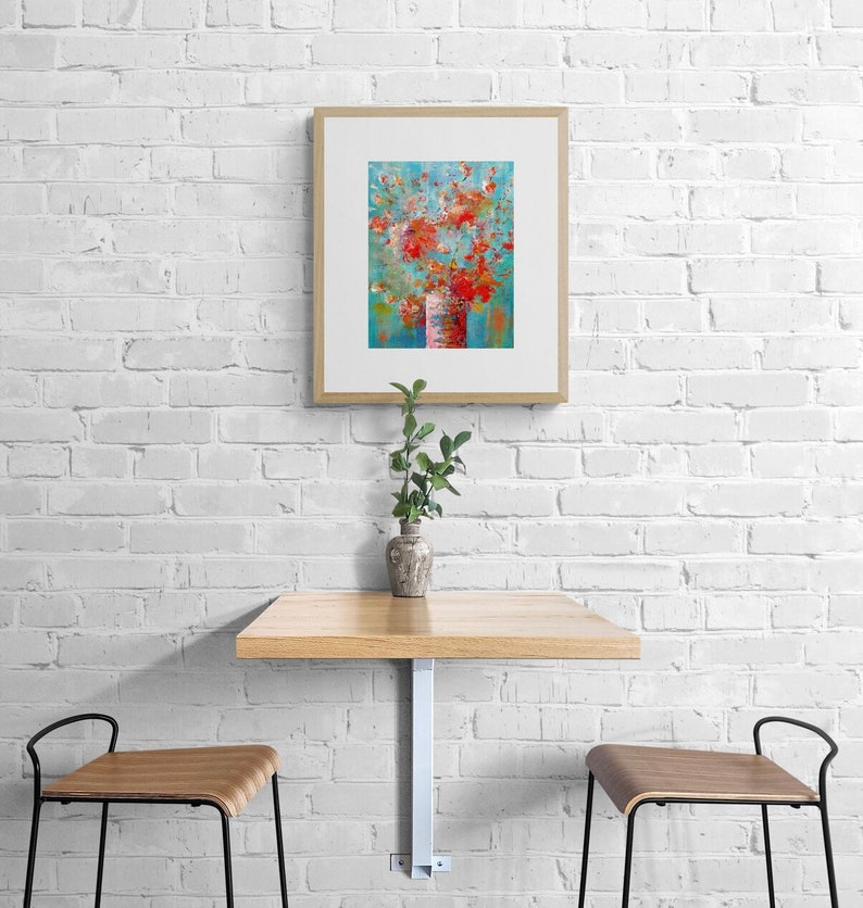 May include: A framed abstract painting of a bouquet of red flowers in a white vase against a blue background. The painting is hanging on a white brick wall above a wooden table with two chairs.