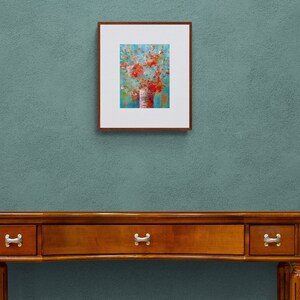 May include: A framed painting of a bouquet of red flowers in a vase against a blue background. The painting is hanging on a wall above a wooden table with drawers.
