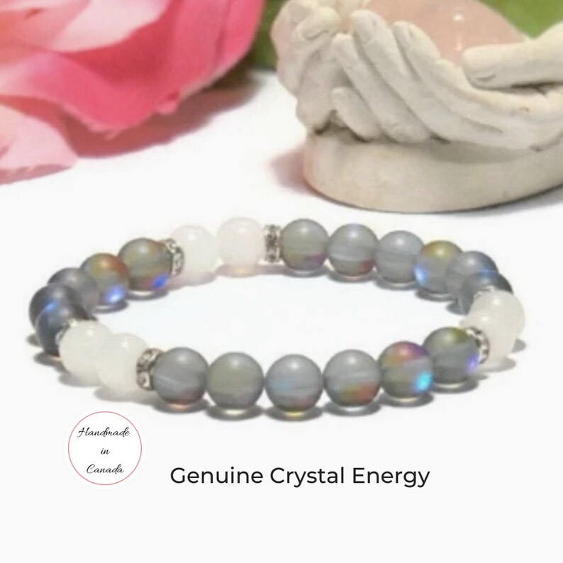 May include: Gray and white crystal beaded bracelet with iridescent accents. The bracelet is handmade in Canada and features the text "Genuine Crystal Energy".