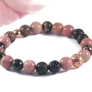 May include: A pink and black beaded bracelet with a rose gold accent. The bracelet is made with pink and black stones and a rose gold charm.