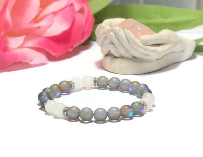 May include: A gray and white beaded bracelet with iridescent beads. The bracelet is made with round beads and has a silver accent.