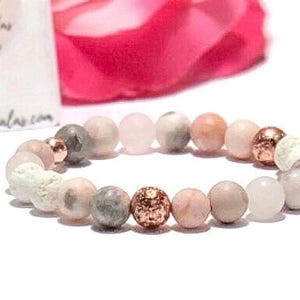 May include: A pink and grey beaded bracelet with rose gold accents. The bracelet is made with natural stones and is designed to be worn on the wrist.