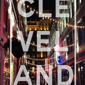 Puede incluir: Una vista nocturna de una calle de la ciudad con la palabra "CLEVELAND" en letras blancas superpuestas sobre la imagen. La calle está bordeada de edificios y decorada con luces de cadena. Hay gente caminando por la acera.