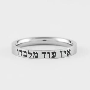 May include: A silver-colored ring with engraved Hebrew text. The ring is a simple band design, with the text wrapping around the exterior. The ring is shown against a plain white background.