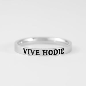 Peut inclure: Une bague anneau en métal argenté poli avec le texte noir gravé VIVE HODIE centré sur la surface extérieure. La bague présente un profil lisse et arrondi ainsi qu'une finition réfléchissante, mettant en valeur des lettres nettes et grasses.