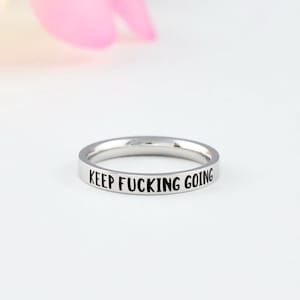 May include: A silver ring with the words "KEEP FUCKING GOING" engraved on the band.