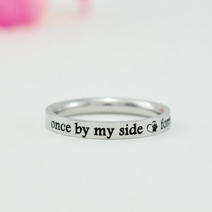 May include: A silver-toned metal ring featuring the engraved black text "once by my side" followed by a small heart symbol containing a paw print, with the word "forever" partially visible at the end of the inscription on the band.