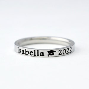 May include: A silver ring with the inscription "Isabella 2022" and a graduation cap symbol.