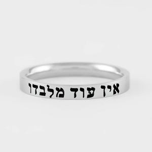 May include: A polished silver-toned band ring featuring a flat outer surface engraved with the Hebrew text "אין עוד מלבדו" in black lettering. The ring has a smooth, reflective finish and a simple, uniform circular shape throughout the band.