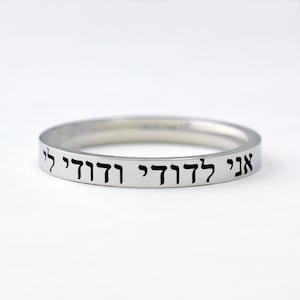 May include: A silver bangle bracelet with the Hebrew phrase "Ani L'dodi V'dodi Li" engraved on it.