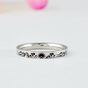 May include: A silver band ring with a black sun and waves design.