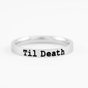 May include: A polished silver-toned metal band ring featuring the text "Til Death" engraved in a bold, black, sans-serif font on the outer surface. The ring has a smooth, reflective finish and a simple, uniform circular design.