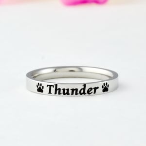 May include: A silver ring with the word "Thunder" engraved on it, flanked by two black paw prints.