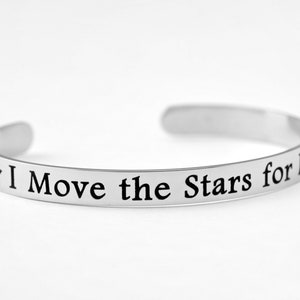 May include: A silver bangle bracelet with the inscription "I Move the Stars for No One" and a small star.