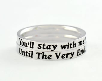 May include: A silver-toned metal ring featuring two stacked bands. The top band is engraved with the black text "You'll stay with me?" and the bottom band is engraved with the black text "Until The Very End." The ring has a smooth, polished finish.