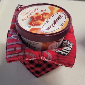 Peut inclure: Un pot de glace Häagen-Dazs dulce de leche dans un protège-bol matelassé rouge et noir. Le protège-bol a un motif de carreaux rouges et noirs et le mot "STATE" en blanc.