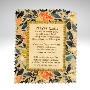 May include: A small, rectangular prayer quilt with a floral pattern in shades of blue, orange, and yellow. The center features text that reads "Prayer Quilt" and a poem. The edges are scalloped, adding a decorative touch to the item.