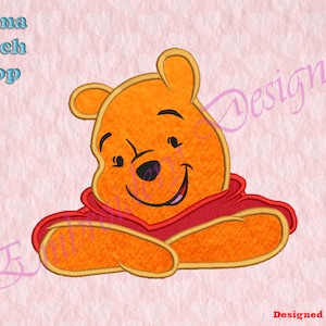 Puede incluir: Diseño bordado de Winnie de Pooh, un oso de dibujos animados con una camisa roja, sonriendo con los brazos cruzados. El diseño está contorneado con hilo dorado.