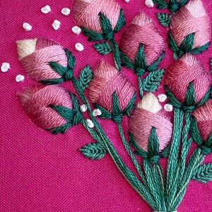 May include: A close-up of a pink and green embroidered bouquet of flowers on a pink fabric background.