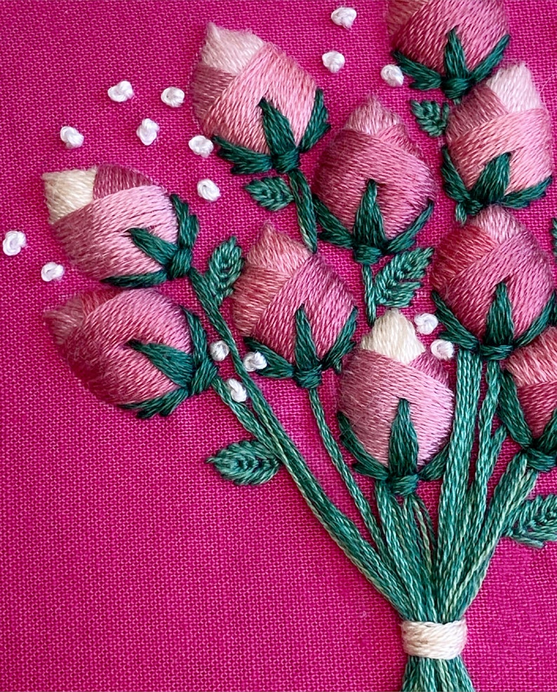 May include: A close-up of a pink and green embroidered bouquet of flowers on a pink fabric background.