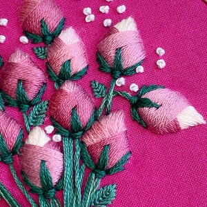 May include: Close-up of a pink fabric with embroidered pink and white flowers with green stems and leaves.