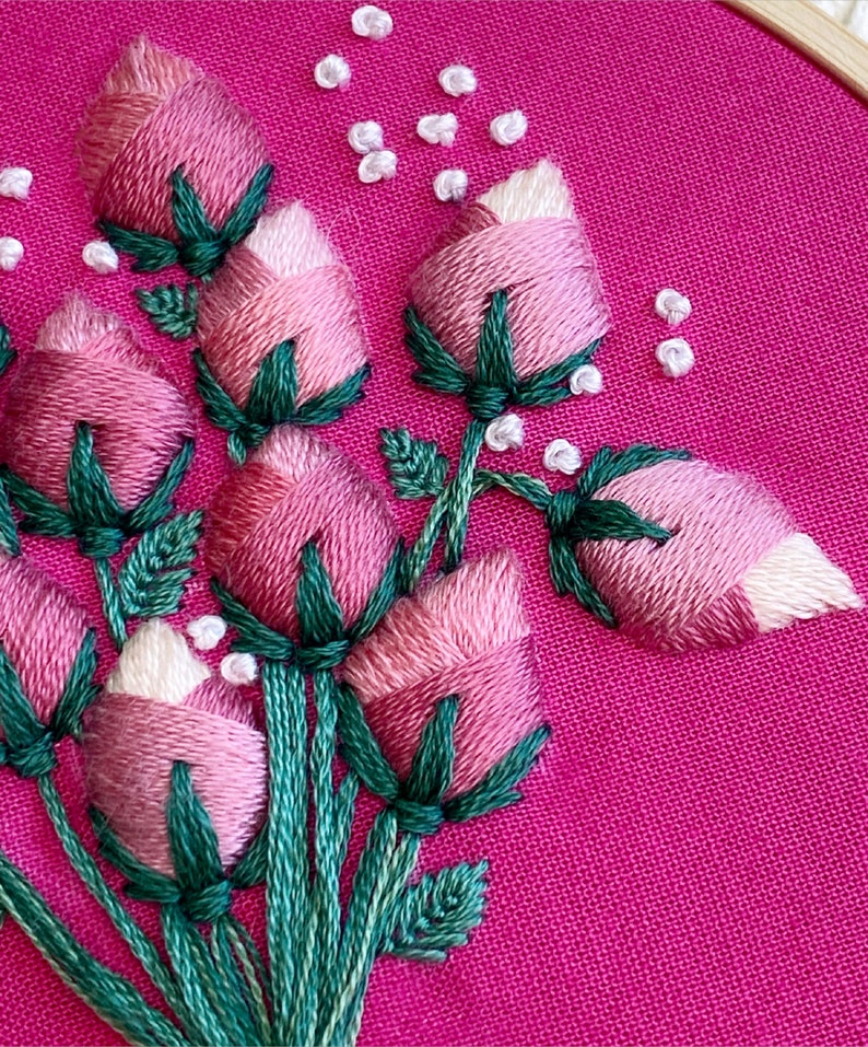 May include: Close-up of a pink fabric with embroidered pink and white flowers with green stems and leaves.