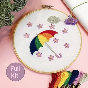 May include: A rainbow embroidery kit featuring a colorful umbrella, a cloud, and pink flowers. The kit includes embroidery floss in various colors and a wooden embroidery hoop. The kit is labeled "Full Kit".