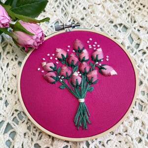 May include: A pink embroidery hoop with a bouquet of pink flowers embroidered on a pink fabric background.