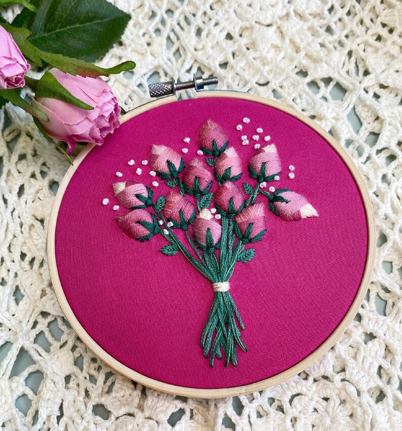 May include: A pink embroidery hoop with a bouquet of pink flowers embroidered on a pink fabric background.