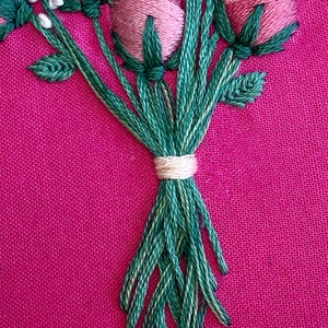 May include: A close-up of a bouquet of pink and white embroidered flowers with green stems tied together with a white ribbon.