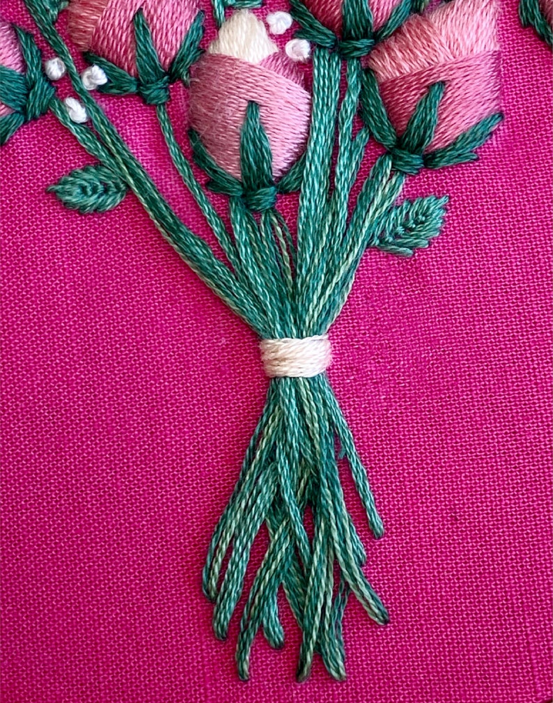 May include: A close-up of a bouquet of pink and white embroidered flowers with green stems tied together with a white ribbon.