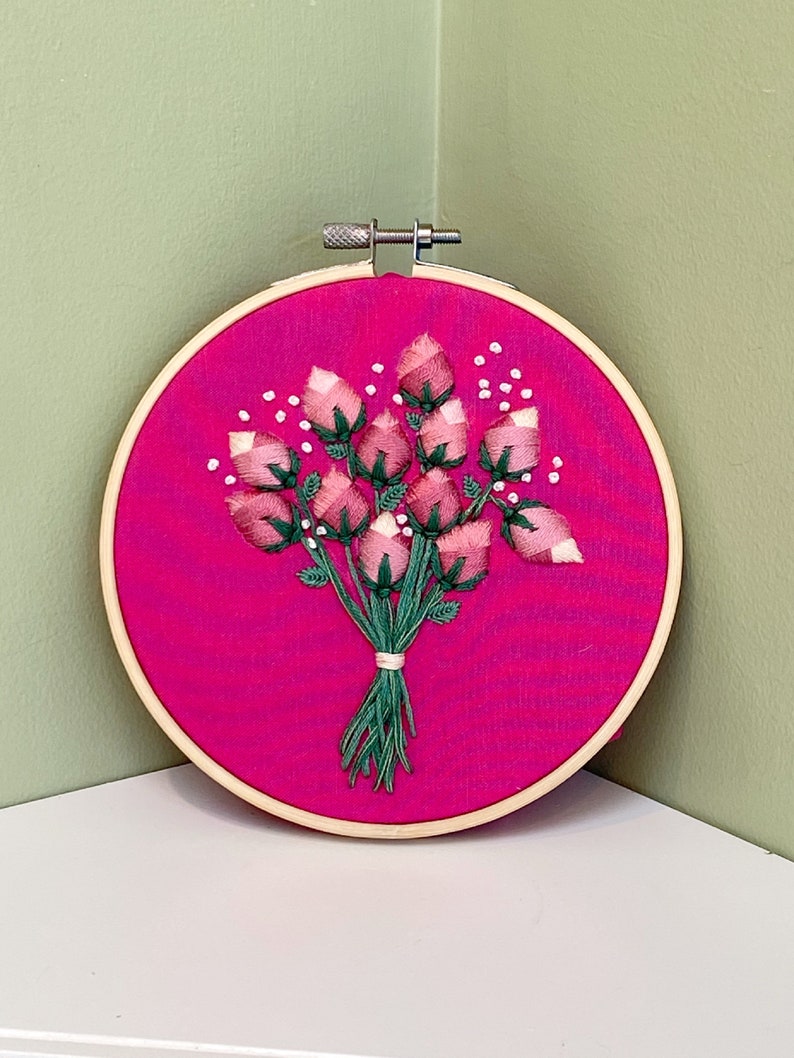 May include: A pink and green embroidered bouquet of roses in a wooden embroidery hoop.