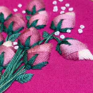 May include: Close-up of a pink fabric with green and white embroidery of a bouquet of flowers. The flowers are pink and white with green leaves.
