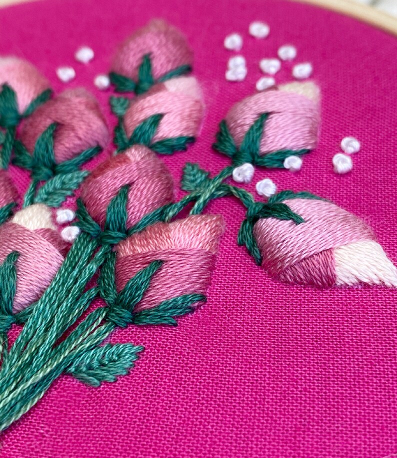 May include: Close-up of a pink fabric with green and white embroidery of a bouquet of flowers. The flowers are pink and white with green leaves.