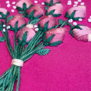 May include: A close-up of a pink and green embroidered bouquet of flowers on a pink fabric background.