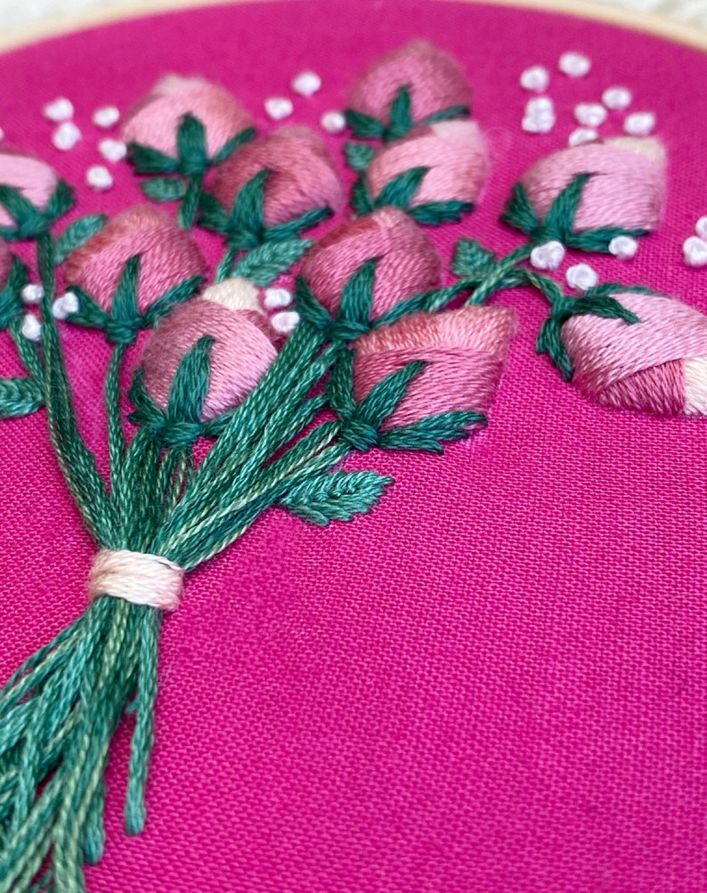 May include: A close-up of a pink and green embroidered bouquet of flowers on a pink fabric background.