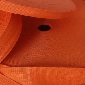 Puede incluir: Primer plano de una cinta de cincha naranja, enrollada y apilada. La cinta es tejida y tiene una superficie texturizada.
