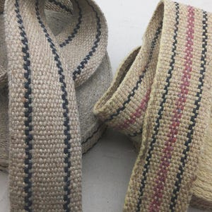 May include: Two rolls of natural colored woven webbing with black and red stripes. The webbing is made of a natural fiber and has a rough texture.