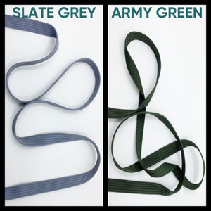 May include: Two lengths of flat woven webbing tape are displayed side by side. The left strip is slate grey, and the right strip is army green. Each piece of fabric tape is arranged in loose, flowing loops against a plain white background.