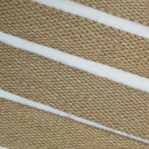 Puede incluir: Primer plano de una tela tejida con rayas blancas. La tela tiene un tono natural, terroso y una textura rugosa.