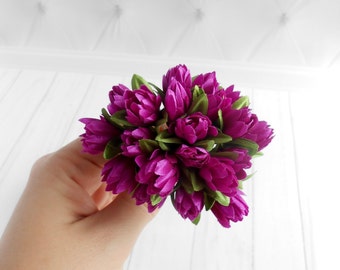 May include: A bouquet of small, deep purple silk flowers with green leaves. The flowers are arranged in a cluster and have a delicate, ruffled appearance.