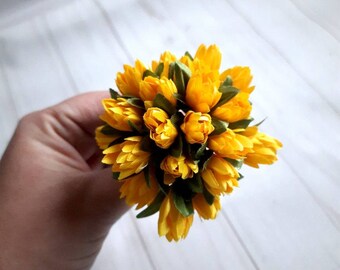 May include: A bouquet of small, bright yellow artificial flowers with green leaves. The flowers are arranged in a circular shape.