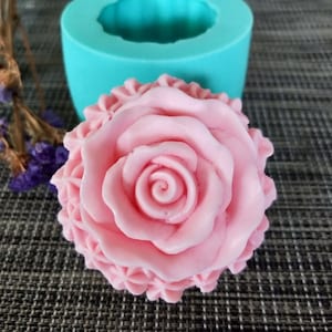 Peut inclure: Un moule à savon en silicone en forme de rose rose. Le moule est bleu sarcelle et a une forme ronde. Le savon est de couleur rose clair et présente un motif de rose détaillé.