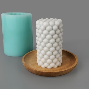 May include: A white candle with a textured, bubble-like surface sits on a wooden tray. A light blue silicone mold is in the background.