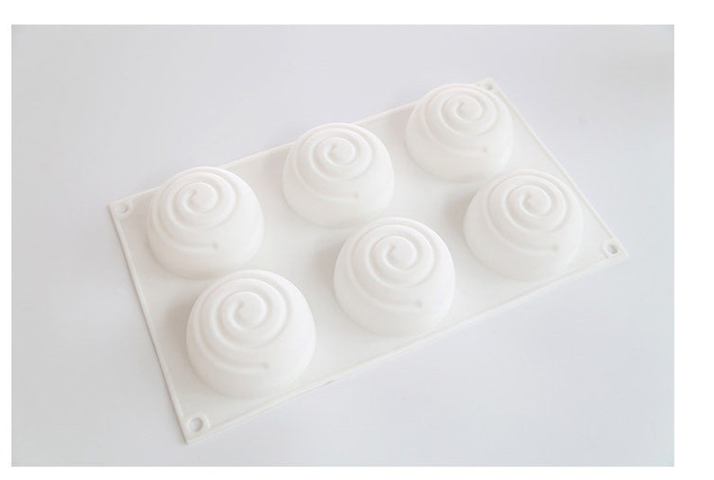 K&ouml;nnte beinhalten: Eine wei&szlig;e Silikonform mit sechs kreisf&ouml;rmigen Vertiefungen, jede mit einem Spiraldesign. Die Form ist rechteckig mit abgerundeten Ecken und f&uuml;r das Backen oder Basteln konzipiert. Die Gesamt&auml;sthetik ist sauber und minimalistisch.